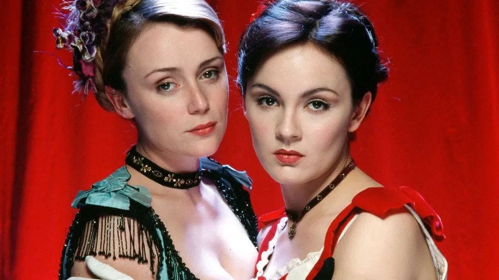 Tipping The Velvet: two women holding eachother close against a red curtain
