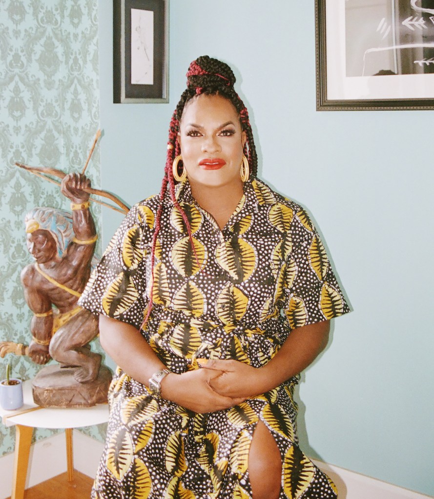 This is an image of a Black trans woman. She is wearing a colourful dress and has her hair in braids. 