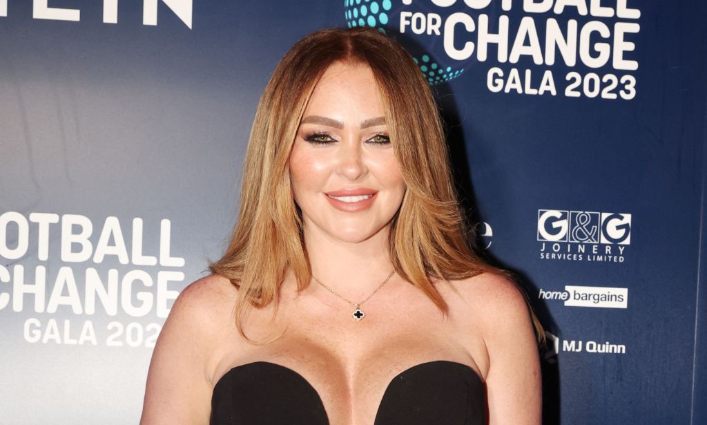 Atomic Kitten star Natasha Hamilton smiles while wearing a black dress at a red carpet event.