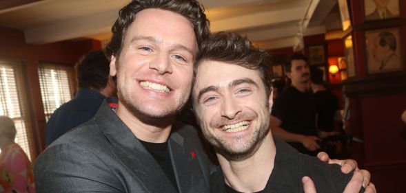 Daniel Radcliffe and Jonathan Groff grab each other and smile as they pose for a photo