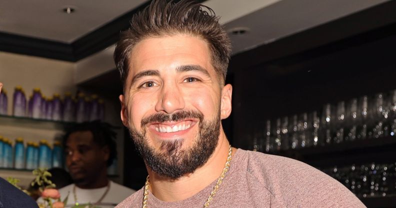 Streamer Nickmercs smiling while wearing a brown top, gold chain and standing in a bar.