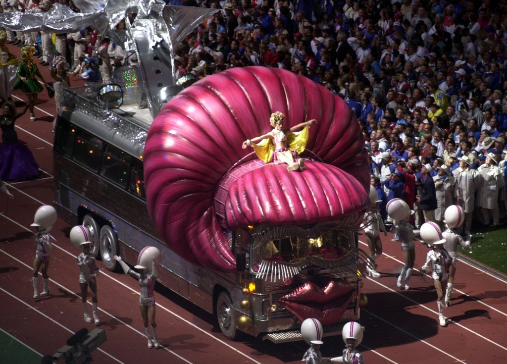 Drag queens strut with a bus, also in drag, at the closing ceremonies of the 2000 Summer Olympics.