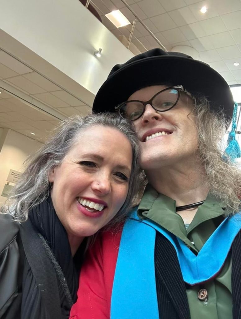 Addy in a graduation gown with her wife Leea.