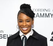 Comedian Amber Ruffin in a black suit jacket, white shirt and black tie. She is smiling while standing on the Grammy 2024 red carpet.