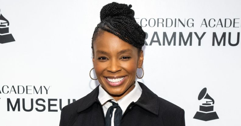 Comedian Amber Ruffin in a black suit jacket, white shirt and black tie. She is smiling while standing on the Grammy 2024 red carpet.