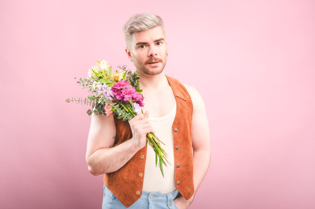 Chris Hall: Girl For All Seasons at Edinburgh Fringe. Chris is holding a boquet of flowers against a baby pink background.