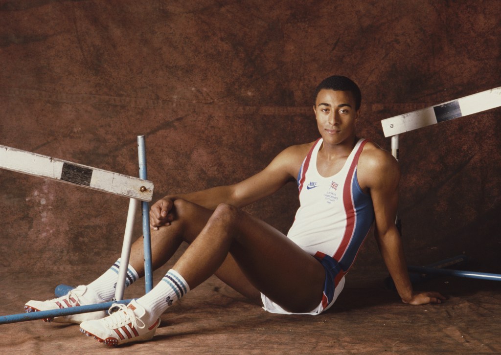 Portrait of hurdler Colin Jackson of Great Britain on 1 June 1987. Colin is sat on the floor against a brown background, in athletic gear, between two hurdles