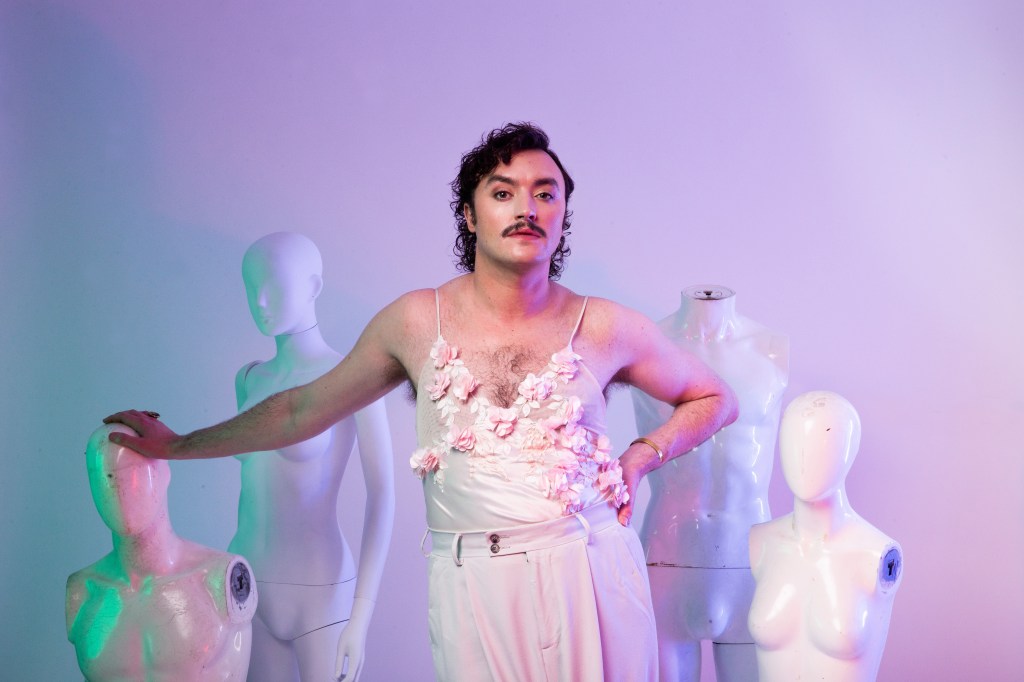 Dan Wye: Dan Wye Am I Sam Smith? at Edinburgh Fringe. Dan is wearing a pink strappy top and trousers, they're leaning on one of the four white manequins without arms and heads.