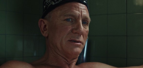 Daniel Craig topless in a bathtub with a black pattened bandana on his forehead.