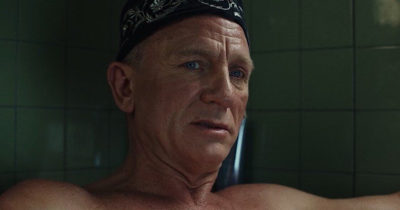 Daniel Craig topless in a bathtub with a black pattened bandana on his forehead.