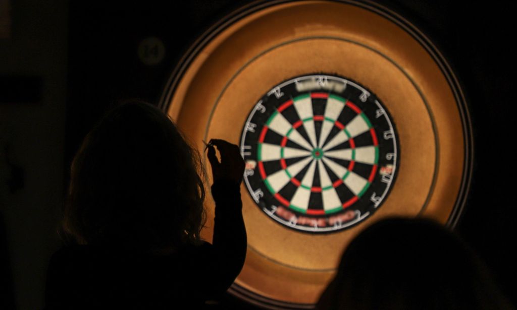 A silhouette throws a dart at a dart board.