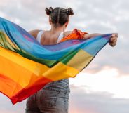 Girl stands holding an LGBTQ+ flag behind her back