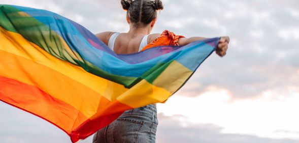 Girl stands holding an LGBTQ+ flag behind her back