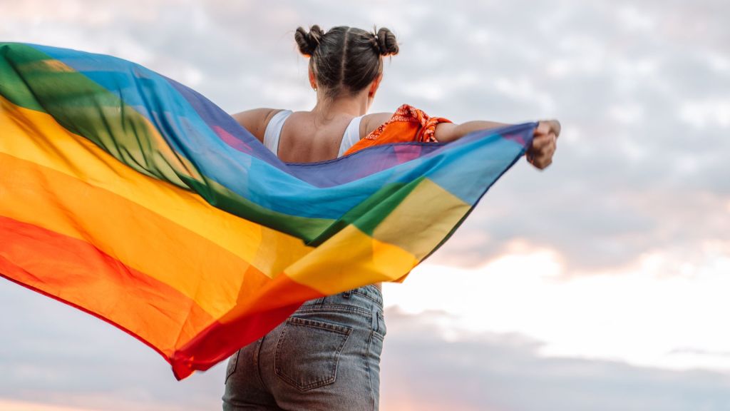 Girl stands holding an LGBTQ+ flag behind her back