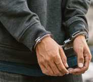 Under arrest, a man's hands with clenched fists are handcuffed behind him.