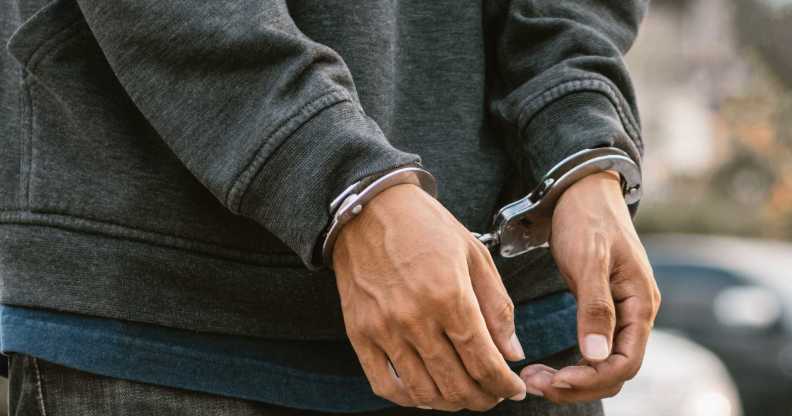 Under arrest, a man's hands with clenched fists are handcuffed behind him.