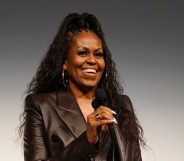 Michelle Obama with a mic smiling in a leather jacket with her hair up.