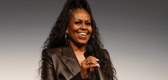 Michelle Obama with a mic smiling in a leather jacket with her hair up.