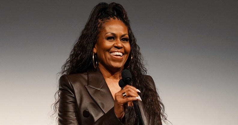 Michelle Obama with a mic smiling in a leather jacket with her hair up.