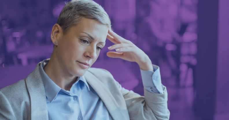 This is an image of an LGBTQ+ professional looking depressed or stressed. She is wearing a khaki suit.