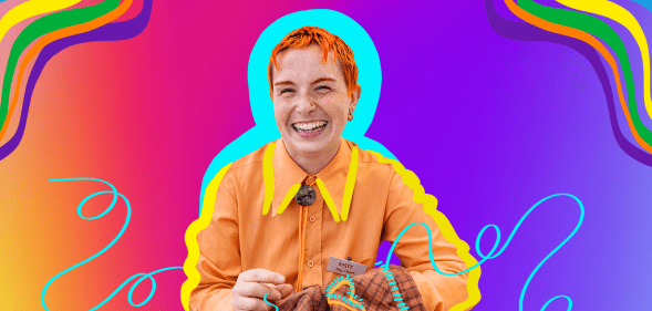 Queer Craft founder Rusty (they/them) smiling in an orange top while holding needlework