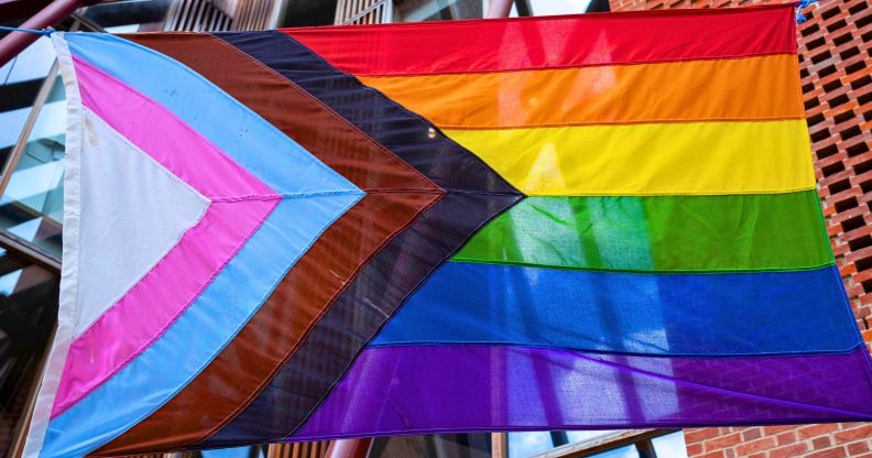 A Progress Pride flag waving in a street.