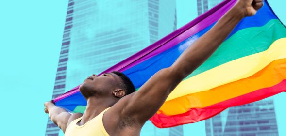 This is an image of a Black man holding a Pride flag in front of an office building
