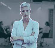 This is an image of an LGBTQ+ professional. She is a woman and she looks frustrated and her arms are folded. In the backgroud there are people in a meeting room.