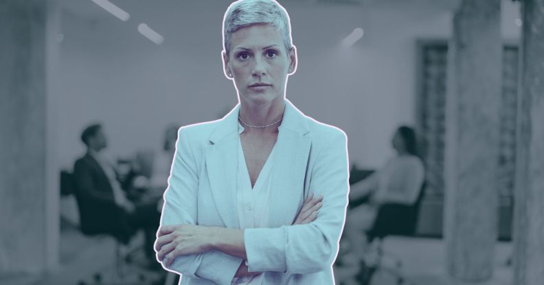 This is an image of an LGBTQ+ professional. She is a woman and she looks frustrated and her arms are folded. In the backgroud there are people in a meeting room.