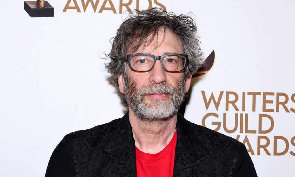 Neil Gaiman in a black blazer, red t-shirt, glasses.