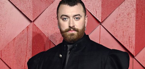 Sam Smith in a black suit posing against a red background.