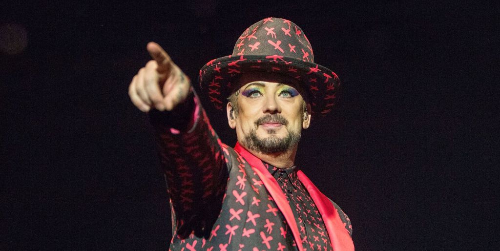 Boy george performing in a red and black patterned outfit and hat