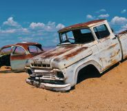 Two car husks sit on the mound of a desert hill.