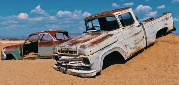 Two car husks sit on the mound of a desert hill.