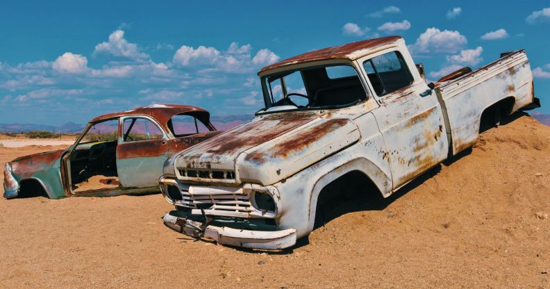 Two car husks sit on the mound of a desert hill.