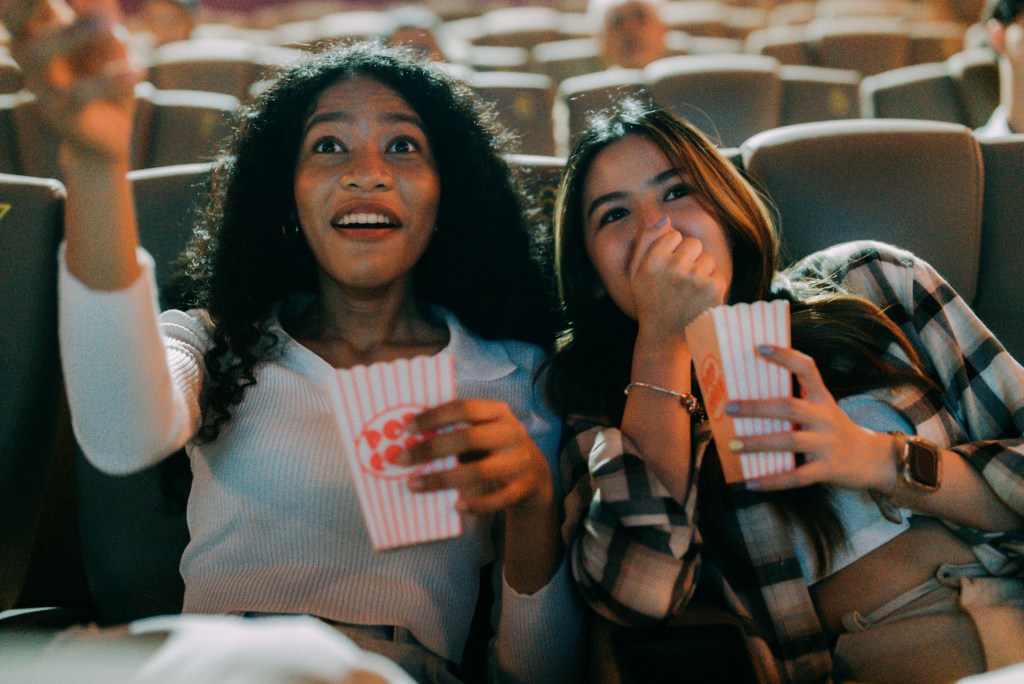 Group of friends of different genders are sitting together chatting happily in a cinema while eating popcorn.