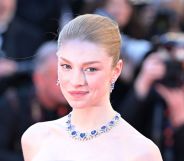 Hunter Schafer on a red carpet in a blue bejewelled necklace.