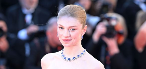 Hunter Schafer on a red carpet in a blue bejewelled necklace.