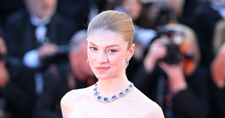 Hunter Schafer on a red carpet in a blue bejewelled necklace.