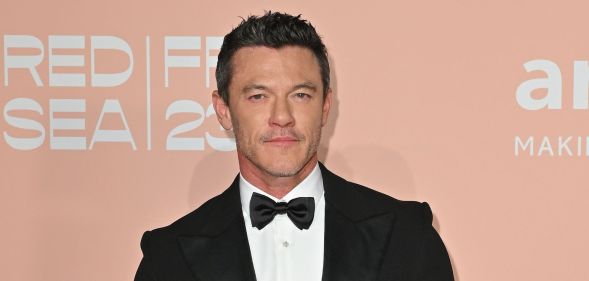 Luke Evans in a black tuxedo and bow tie against a peach background