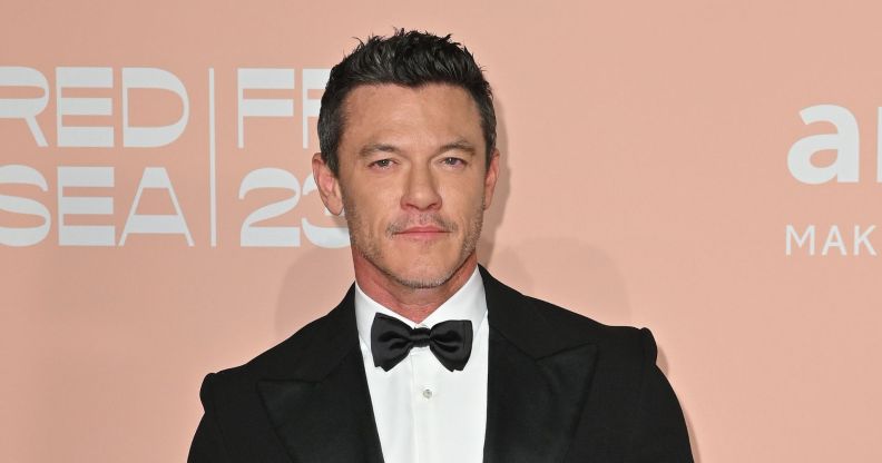 Luke Evans in a black tuxedo and bow tie against a peach background