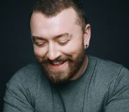 Sam Smith smiling wearing a grey top and looking down.
