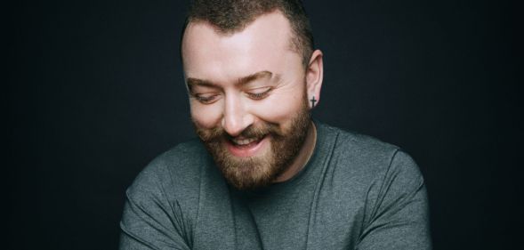 Sam Smith smiling wearing a grey top and looking down.