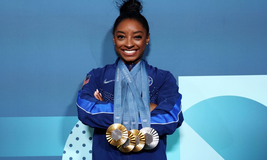 Simone Biles pictured with three gold medals and one silver medal around her neck.