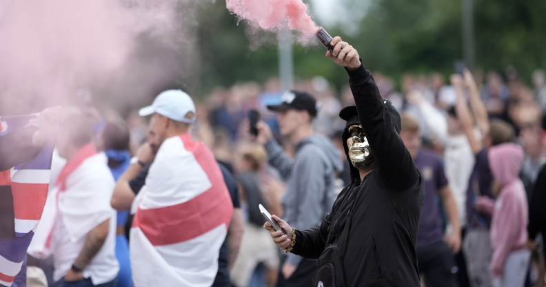 ROTHERHAM, ENGLAND - AUGUST 4: An anti-migration protester holds a flare during a riot outside of the Holiday Inn Express in Manvers, which is being used as an asylum hotel, on August 4, 2024 in Rotherham, United Kingdom. Yesterday saw widespread violence as Far-right agitators in Liverpool and Manchester rioted and looted shops. Police were attacked and injured and dozens of arrests were made. (Photo by Christopher Furlong/Getty Images)