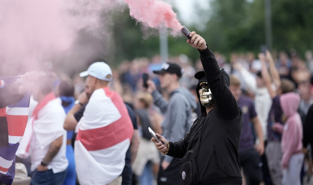 ROTHERHAM, ENGLAND - AUGUST 4: An anti-migration protester holds a flare during a riot outside of the Holiday Inn Express in Manvers, which is being used as an asylum hotel, on August 4, 2024 in Rotherham, United Kingdom. Yesterday saw widespread violence as Far-right agitators in Liverpool and Manchester rioted and looted shops. Police were attacked and injured and dozens of arrests were made. (Photo by Christopher Furlong/Getty Images)