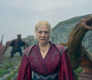 Rhaenyra dressed in a red robe with 2 roaring dragons behind her.