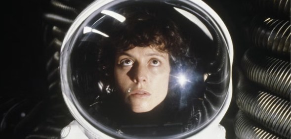 Actors Sigourney Weaver in a space suit looking up.