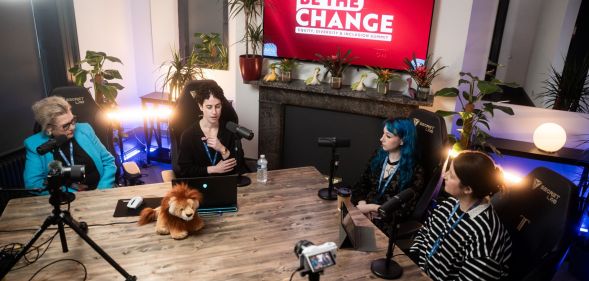 This is an image of a panel discussion. There are 4 speakers in total, and they are sitting at a large table with microphones and cameras set up.