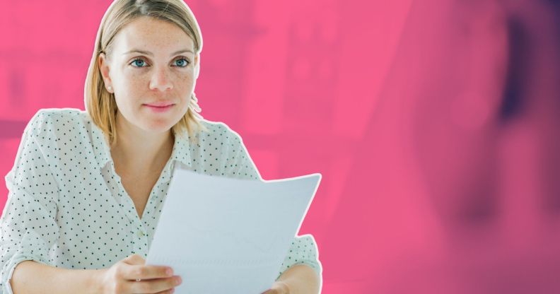 This is an image of a white woman with shoulder length blond hair holding a piece of paper. The background is a blurred out meeting room and is stylised in fuschia.